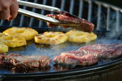 Cropped image of hand cooking meat on barbecue grill