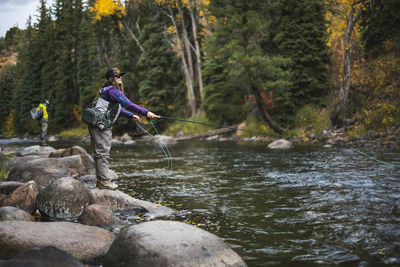 Side view of woman fly fishing while standing on rock at roaring fork river