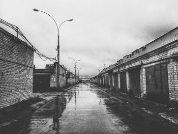 Wet street amidst buildings against sky in city