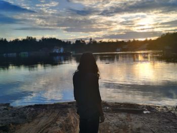 Rear view of man standing by lake against sky during sunset