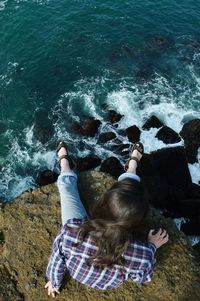 Rear view of women sitting on rock over sea