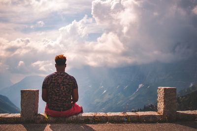 Rear view of man sitting on mountain against sky