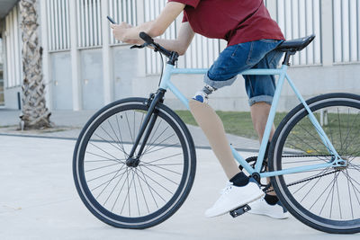 Young male with leg prosthesis sitting on bike and messaging