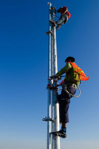 Low angle view of people working against clear blue sky