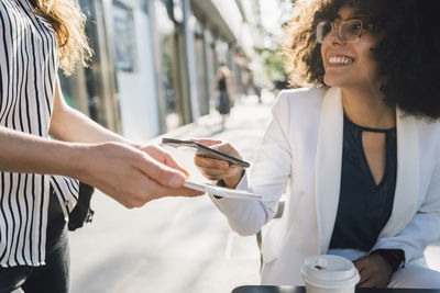 Young businesswoman paying through smart phone at sidewalk cafe