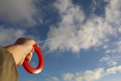 Cropped hand of boy flying kite against sky