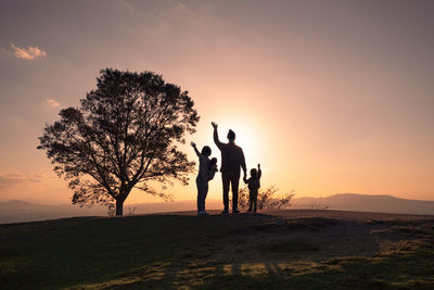 Silhouette people standing on land against sky during sunset