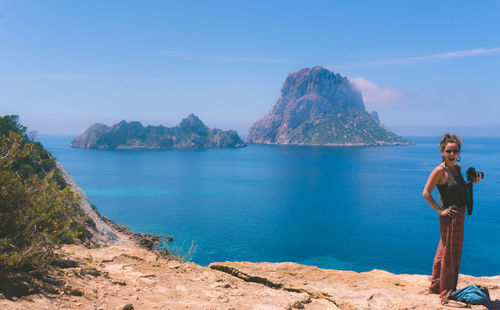 Man standing on rock by sea against sky