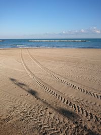 Tire tracks on beach against sky