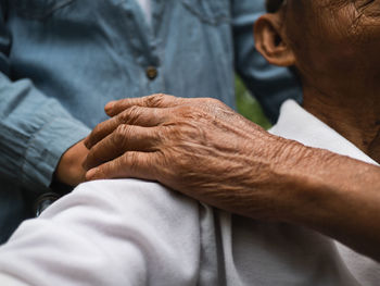 Close-up hand of granddaughter holding grandfather's shoulder in a wheelchair in the park. 