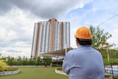 Rear view of man standing by building against sky
