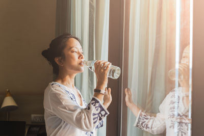 Side view of woman drinking glass at home