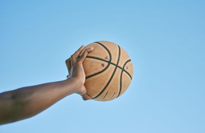 Low angle view of hand holding basketball against clear blue sky