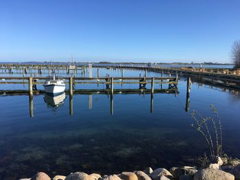 Wooden posts in calm lake against clear blue sky