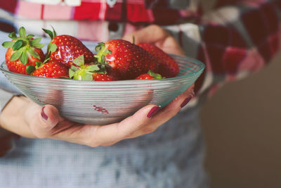 Midsection of woman holding strawberries in bowl