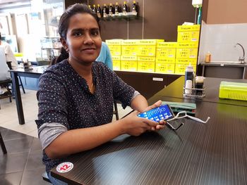 Portrait of young woman using mobile phone while sitting at wooden table in cafe