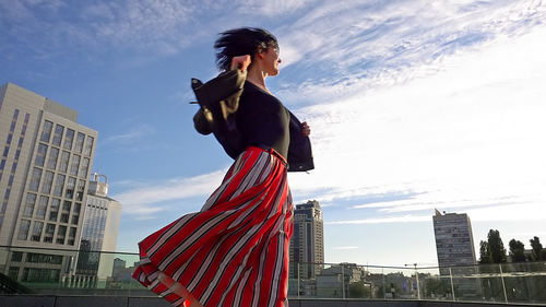 Low angle view of young woman standing in city against sky