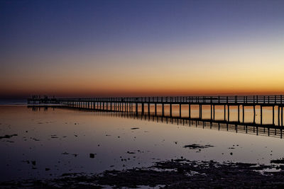 Pier on sea against clear sky at sunset