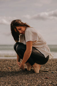 Full length of woman crouching on beach against sea