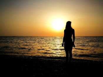 Silhouette man standing on beach against sky during sunset