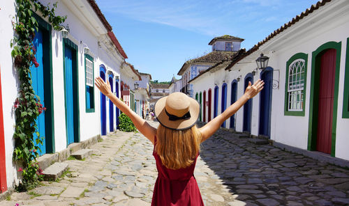  beautiful young woman with raised arms walking in colorful historic town of paraty, brazil.