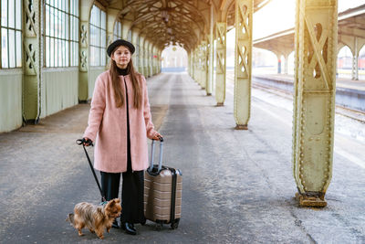Empty station building. young woman passenger stands with suitcase and small