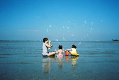 Family sitting at beach against clear blue sky during sunny day