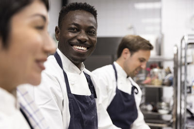 Portrait of smiling chef amidst colleagues working in kitchen at restaurant