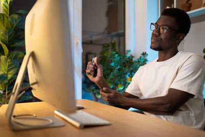 Young african american man takes care of hand wrist using expander during long time work on computer