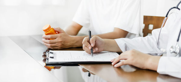 Midsection of doctor writing in book