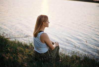 Side view of woman sitting on land by lake 