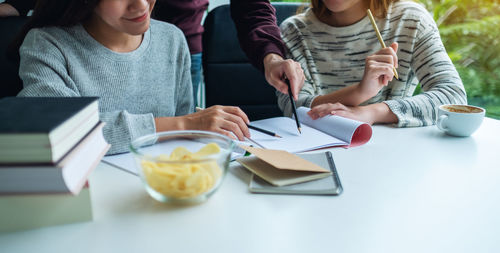 Group of young students tutoring and catching up workbook with friends