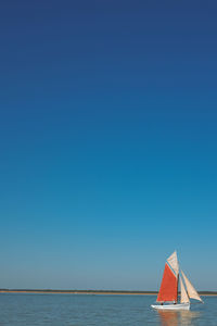 Sailboat sailing in sea against clear blue sky