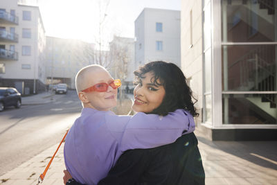 Smiling female friends or gay couple hugging and looking at camera