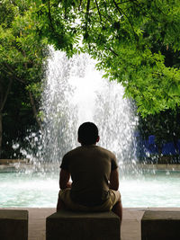 Rear view of man sitting against fountain at park