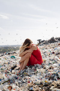 Woman sitting amidst garbage against sky