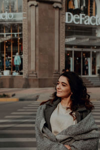 Woman looking away while standing against building