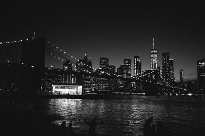 Illuminated bridge over river by buildings against sky at night