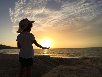 Rear view of silhouette woman standing at beach during sunset