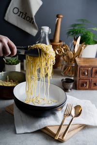 Cropped hand of person holding noodles with serving tongs on table