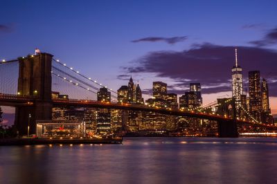 Brooklyn bridge over river against illuminated cityscape during dusk