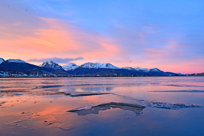 Scenic view of lake by snowcapped mountains against sky during sunset