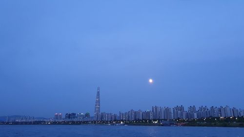 Illuminated buildings by sea against clear blue sky