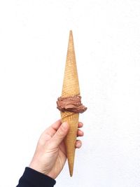 Cropped hand holding ice cream against wall