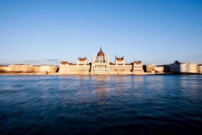 Hungarian parliament building by danube river against clear blue sky in city