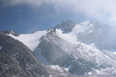 Alpine pointed peaks of mountains covered with snow in clouds, fog and sunlight in winter