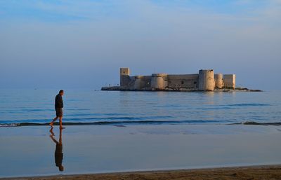 Rear view of man standing in sea against sky