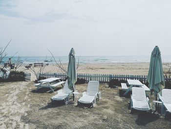 Deck chairs on beach against sky