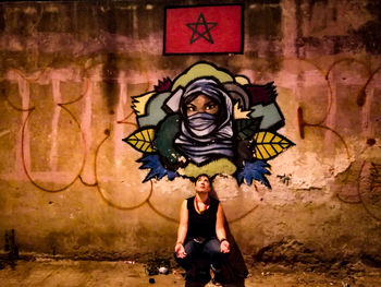 Woman crouching against graffiti wall at night