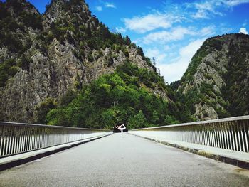 Footbridge amidst trees and mountains against sky